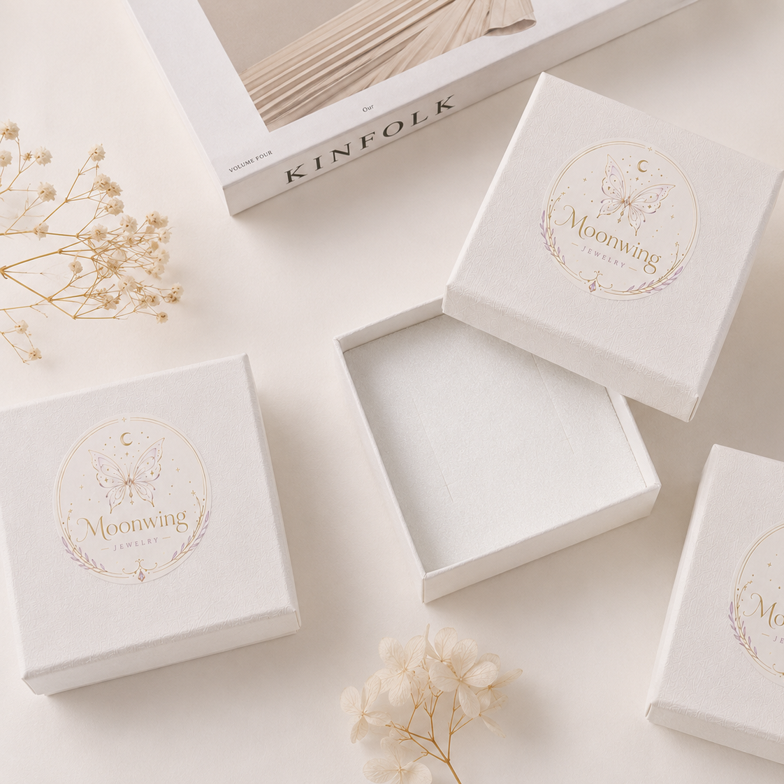closed box with a gold circular 'Moonwing' logo. Dried flowers and a white ceramic dish are styled around them.