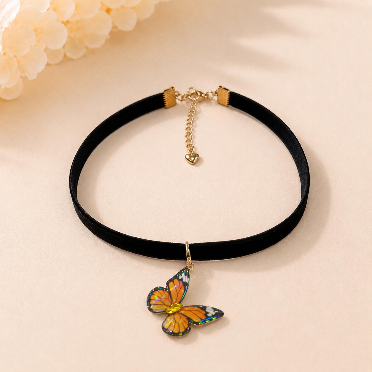 A black velvet choker necklace with a gold-tone butterfly pendant, displayed on a light beige background with soft decorative flowers in the corner.