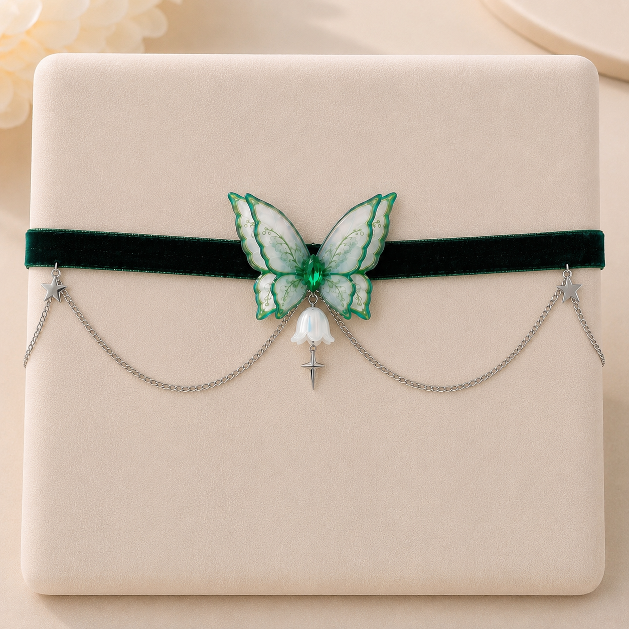 A dark green velvet headband with a central green and white butterfly embellishment, silver dangling chains, and a small white bell-shaped charm, displayed on a beige jewelry box.