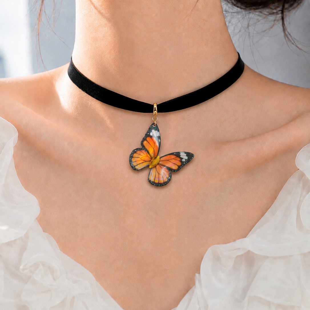 A close-up of a model wearing a black velvet choker necklace with a dangling butterfly pendant. The butterfly pendant features orange, black, and white patterned wings with a small gold-colored metal connector.